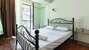 Une chambre avec un lit en métal, une fenêtre avec des rideaux et une vue sur l’extérieur.