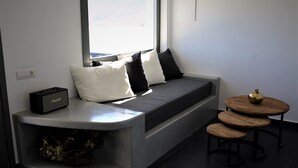 A modern living room with a built-in bench, a small table with a decorative apple, and a speaker on the bench. - A Lux Villas Santorini (Santorini)