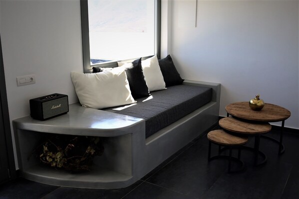 A modern living room with a built-in bench, a small table with a decorative apple, and a speaker on the bench. - A Lux Villas Santorini (Santorini)