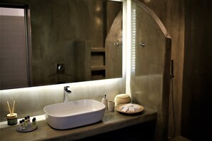 Een moderne badkamer met een grote spiegel, een witte wastafel en diverse toiletartikelen op het aanrecht.
