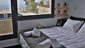 A bedroom with a bed, a window with a view of the landscape, and a shelf with books and a cactus. - A Lux Villas Santorini (Santorini)