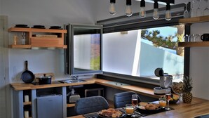 A modern kitchen with a dining area, a refrigerator, a sink, and a window with a view of greenery. - A Lux Villas Santorini (Santorini)