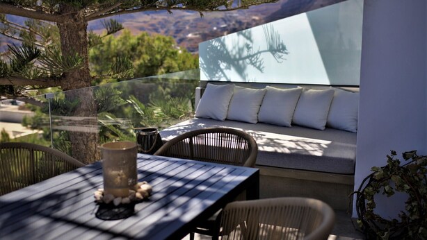 A glass-enclosed outdoor seating area with a table, chairs, and a cushioned bench. - A Lux Villas Santorini (Santorini)