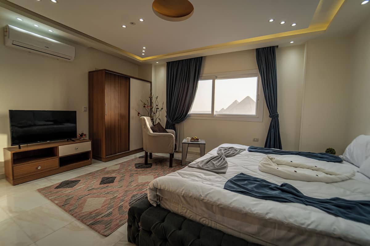 A modern bedroom with a large bed, a TV, a wardrobe, a chair, a small table, and a window with curtains.