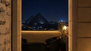 Un balcón con vista a una pirámide de noche, una mesa, sillas y una pared con ilustraciones.