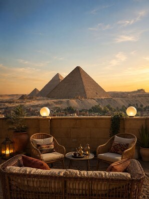 A terrace with wicker furniture, a table with a teapot, and a view of the pyramids. - Gardenia Pyramids View Inn - Rooftop (Giza)