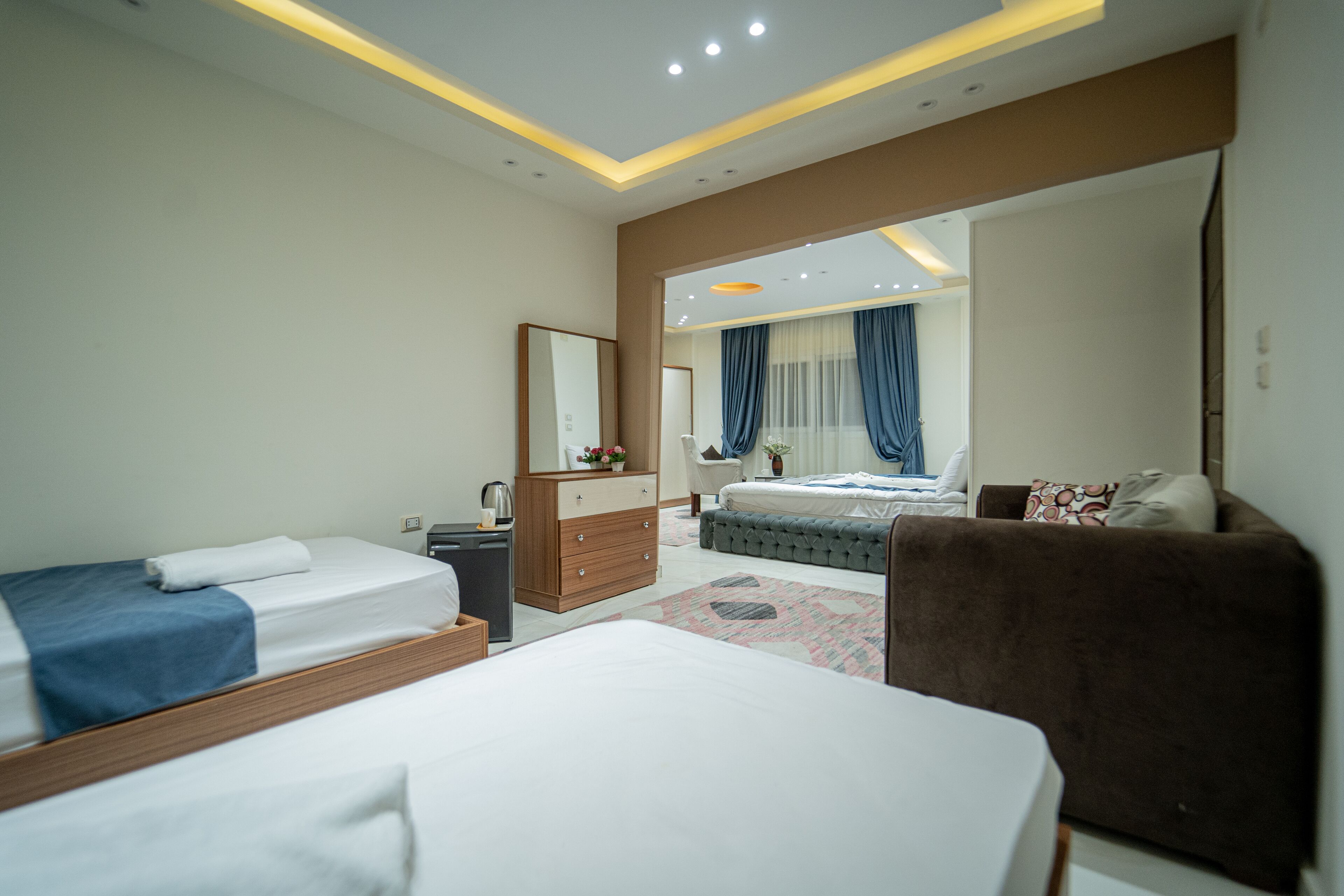 Une chambre d’hôtel moderne avec deux lits, un canapé, une commode et un grand miroir.