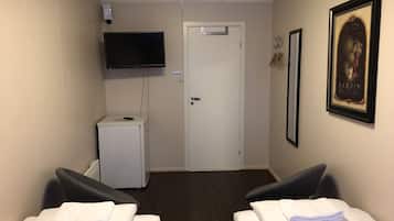 A hotel room with two beds, a television mounted on the wall, a small white cabinet, and a door with a sign above it.