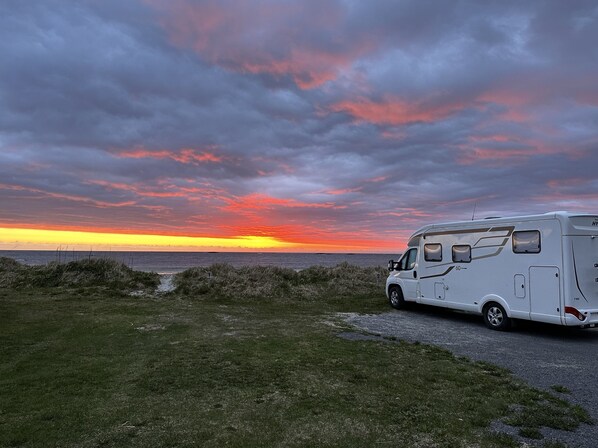A white RV parked on a grassy area with a sunset in the background.