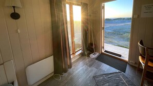 A room with a view of the beach, a door with a 'No Dogs in the Beds' sign, a lamp, and a chair. - Midnattsol rom og hytter (Andoy)