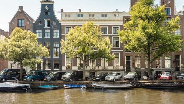 Un canal bordé de bateaux amarrés, une rangée de bâtiments traditionnels en briques et des voitures garées le long du quai.