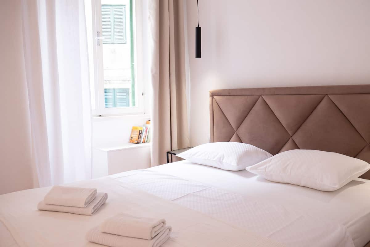 A neatly made bed with a tufted headboard, white linens, and two folded towels on the bed.