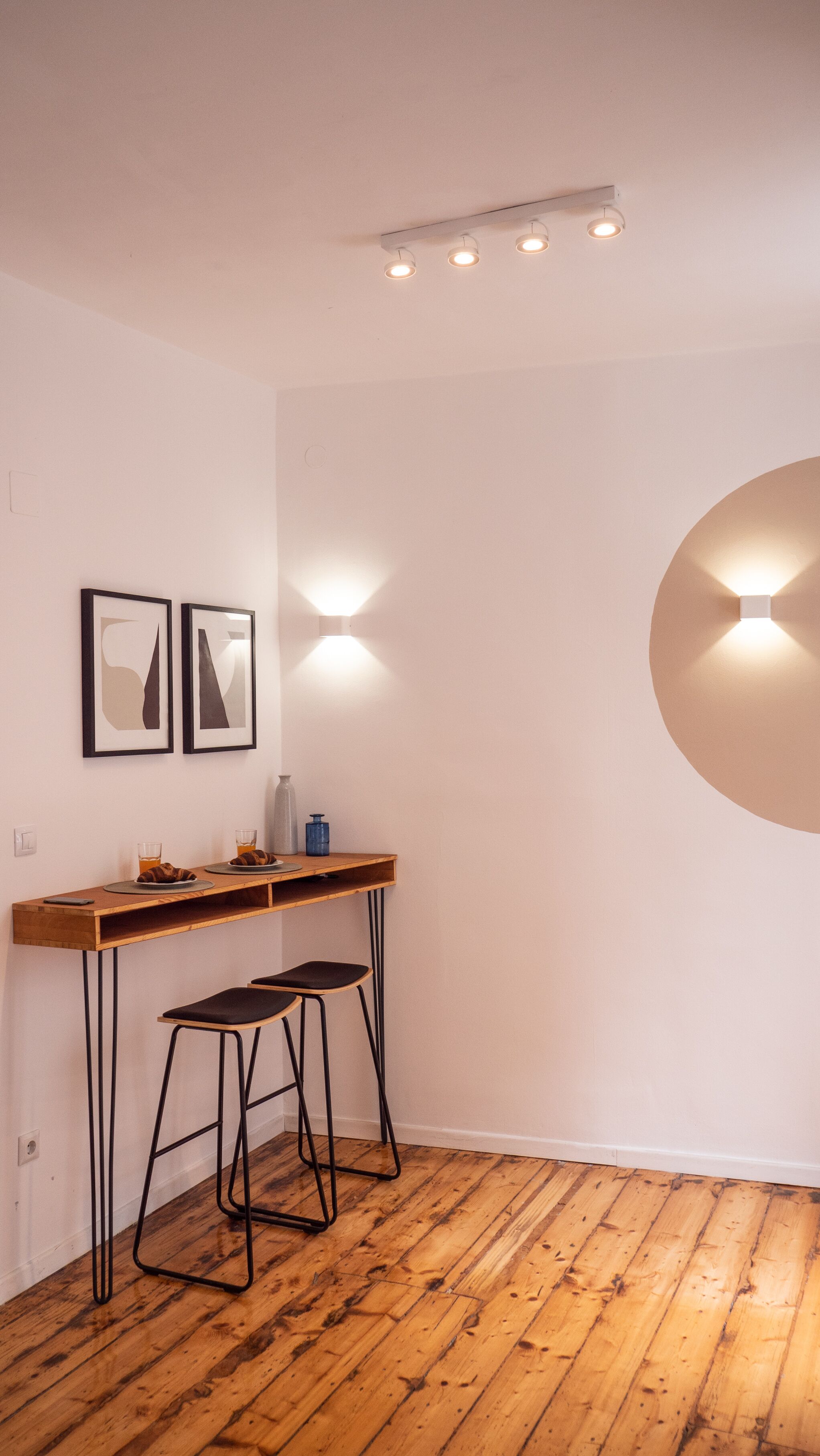 A modern kitchen with a wooden countertop, two bar stools, and a wall-mounted light fixture.