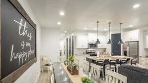 A modern kitchen with white cabinets, a central island with seating, and a chalkboard with a message. - 3BR Sleeps 18 w/ 3 Kings & Bunk Loft - Near Pool (St. George)