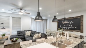 A modern kitchen with a granite countertop, stainless steel sink, and pendant lighting. There is a dining area with a white table and chairs. - 3BR Sleeps 18 w/ 3 Kings & Bunk Loft - Near Pool (St. George)