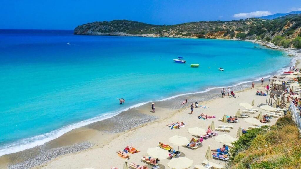 A beach with clear turquoise waters, a sandy shore, and a few boats.