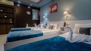A hotel room with two beds, each with a blue bedspread and white pillows, and a decorative swan on each bed. There is a nightstand with a lamp, a wall-mounted mirror, and a shelf with plants. - Cloud 9 Hotel Shisha & Cocktail Bar - Adults Only (Hersonissos)