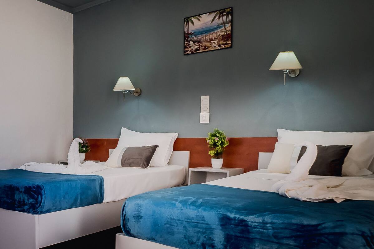 Une chambre d’hôtel avec deux lits, une table de chevet avec une lampe, un luminaire fixé au mur et un tableau au-dessus des lits.