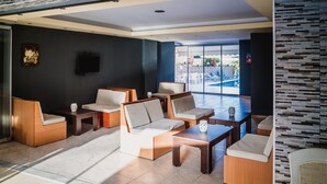 A modern lounge area with sofas and tables, a flat-screen TV, and a view of an outdoor pool. - Cloud 9 Hotel Shisha & Cocktail Bar - Adults Only (Hersonissos)