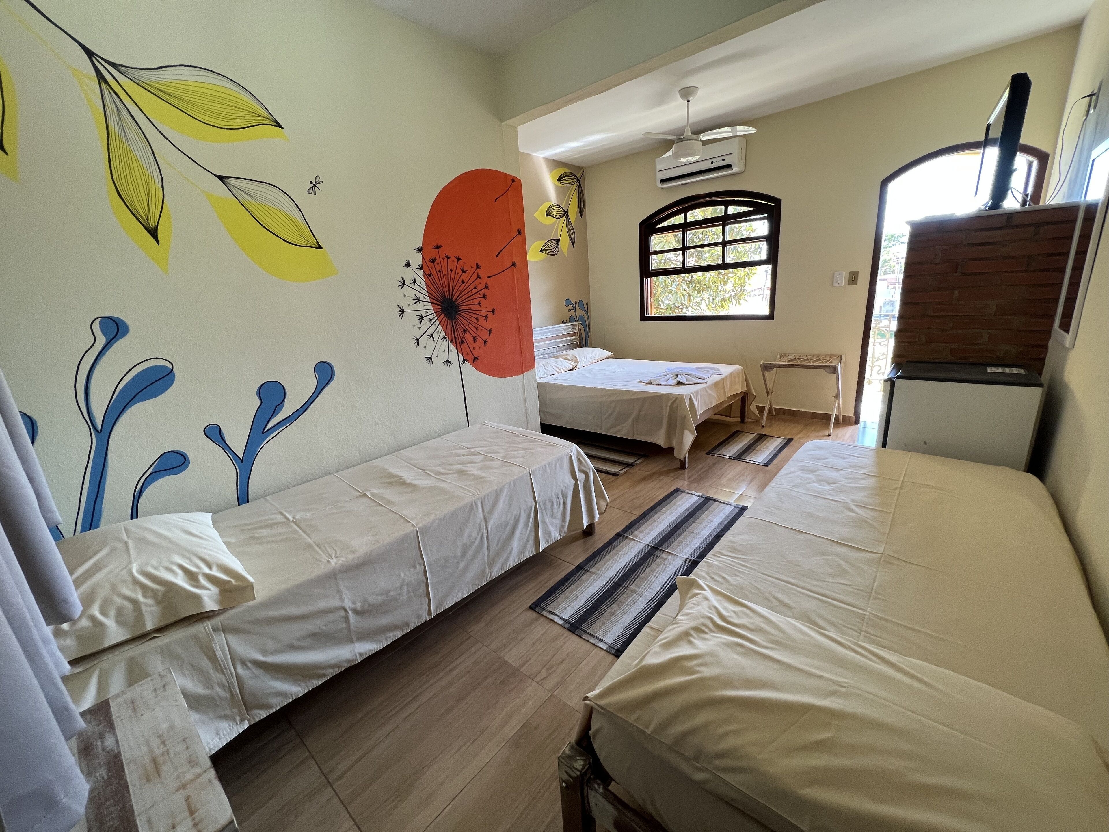 Una habitación con dos camas, una ventana, ventilador de techo y chimenea de ladrillo.