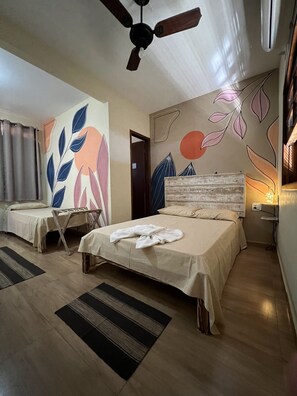 A hotel room with two beds, a ceiling fan, a wall with abstract art, and a bedside table with a lamp.