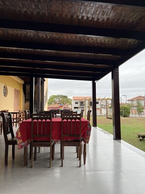 An outdoor covered dining area with a brick ceiling, wooden tables and chairs, and a view of the surrounding neighborhood.