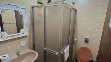 Un baño con lavamanos, espejo, cabina de ducha, inodoro y toallero.