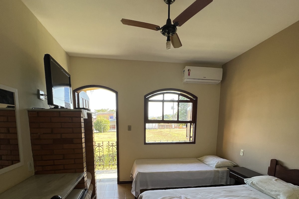 A hotel room with two beds, a TV, a ceiling fan, and a window.