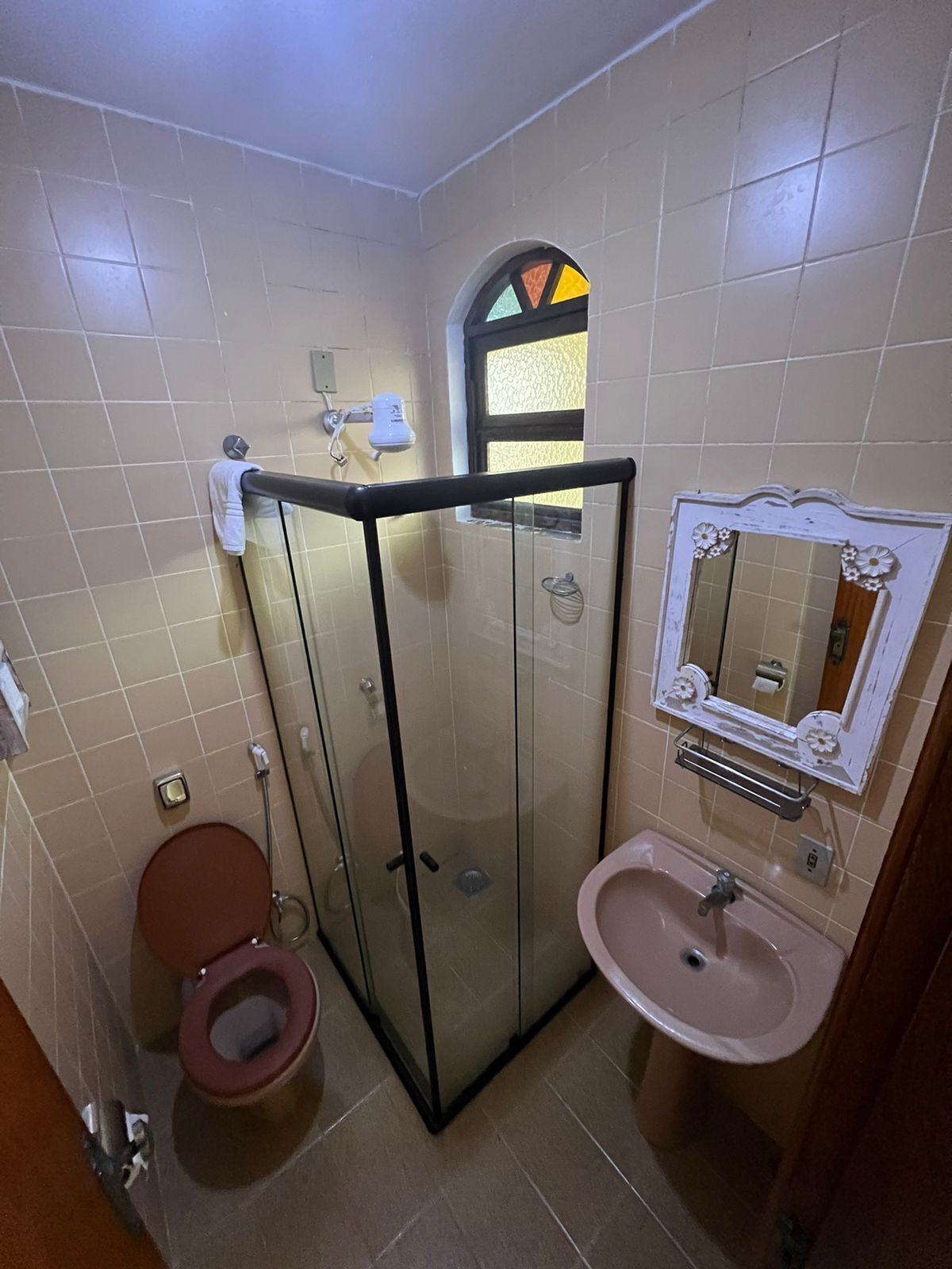 A bathroom with a glass-enclosed shower, a toilet, and a sink with a decorative mirror.