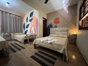 A hotel room with two beds, a small table, a chair, and a wall with leaf patterns.