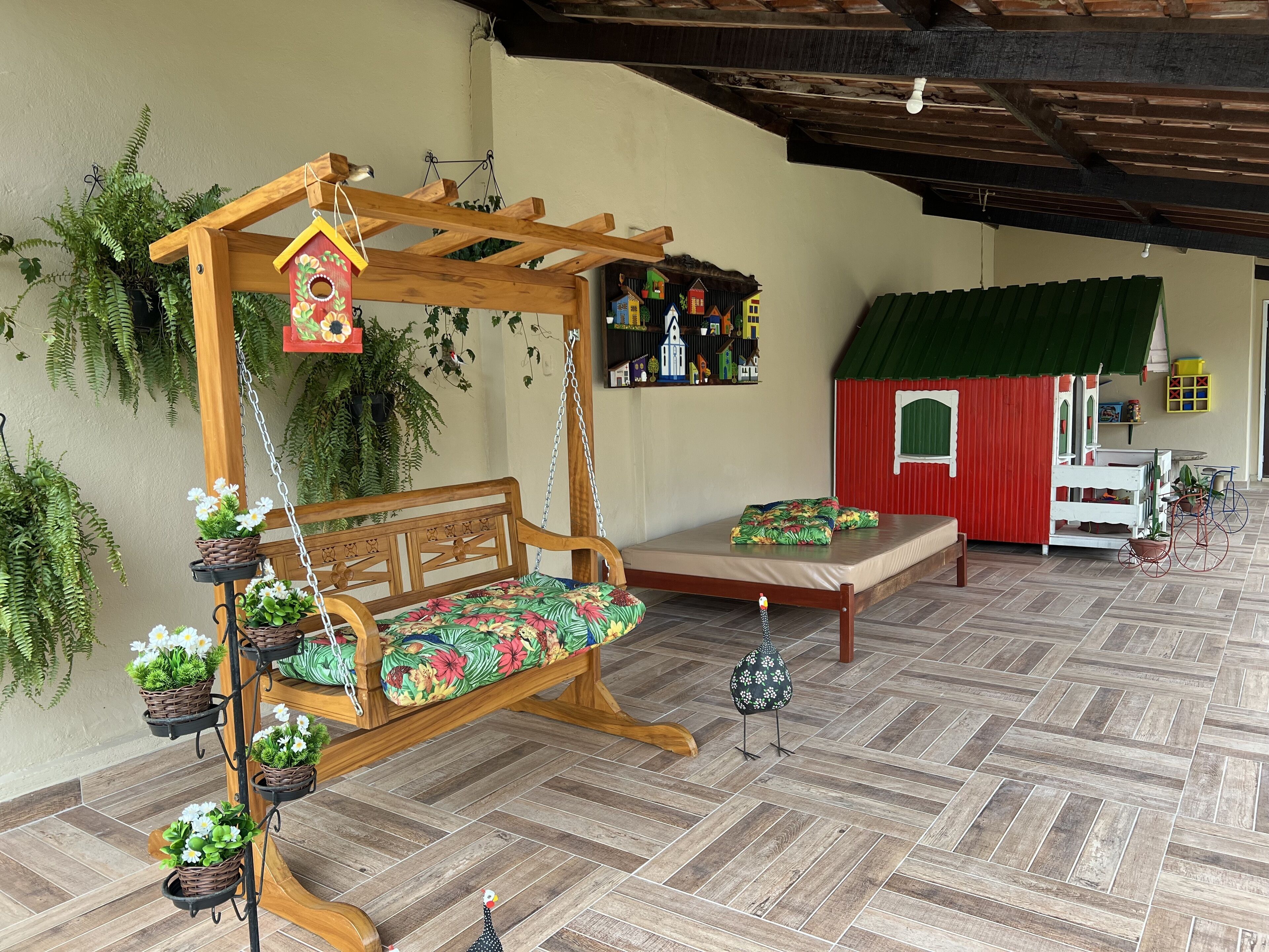 A wooden swing with a cushioned seat, a small birdhouse, and a red playhouse.
