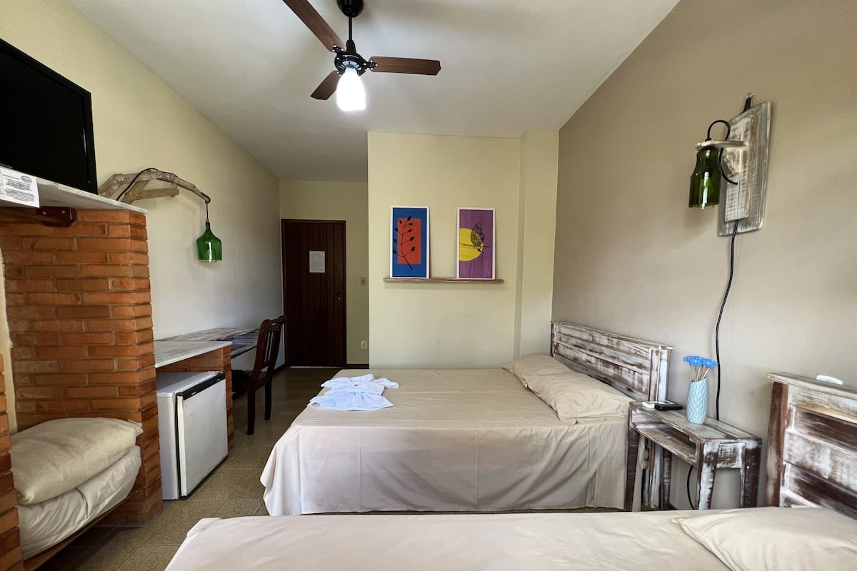 A hotel room with two beds, a desk, a chair, a small refrigerator, and a ceiling fan.