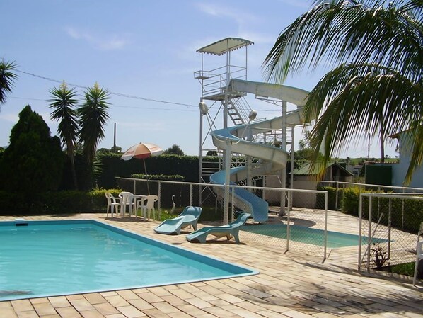 A swimming pool with a water slide, lounge chairs, and palm trees.