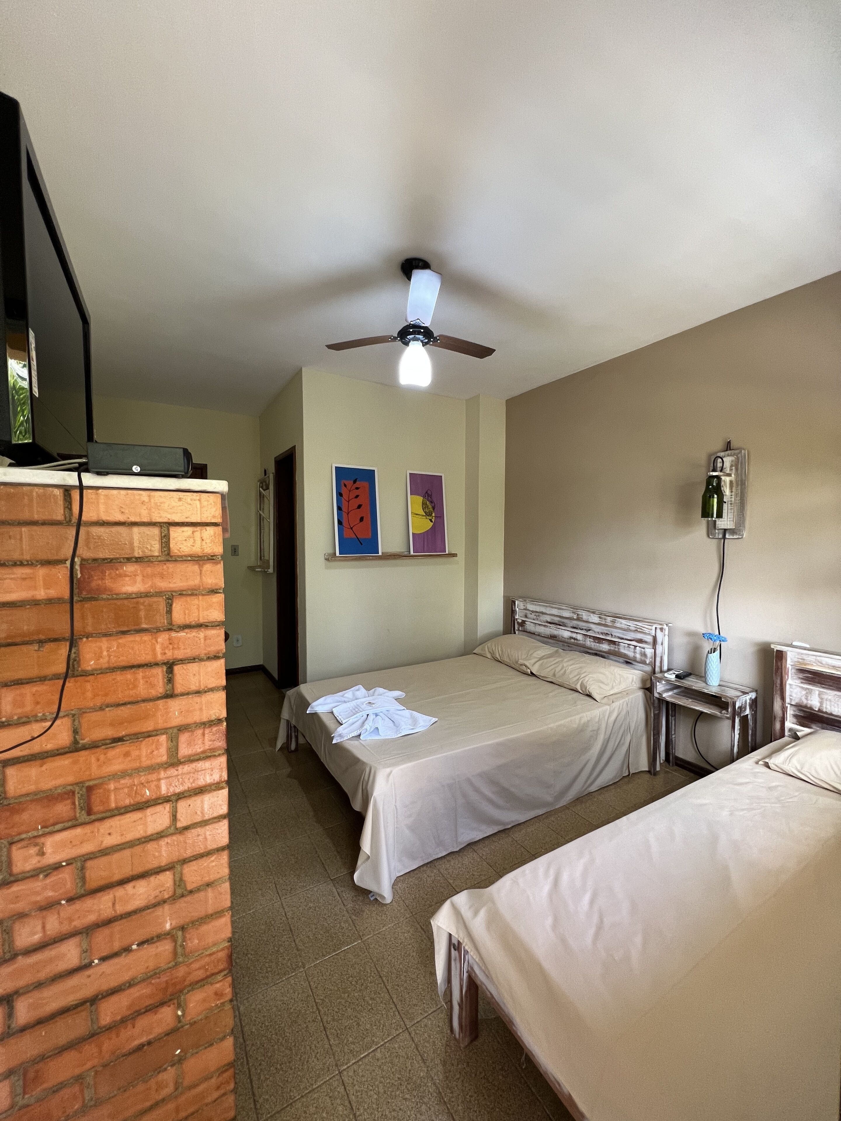 Habitació d'hotel amb dos llits, una paret de maó, un ventilador de sostre i obres d'art a la paret.