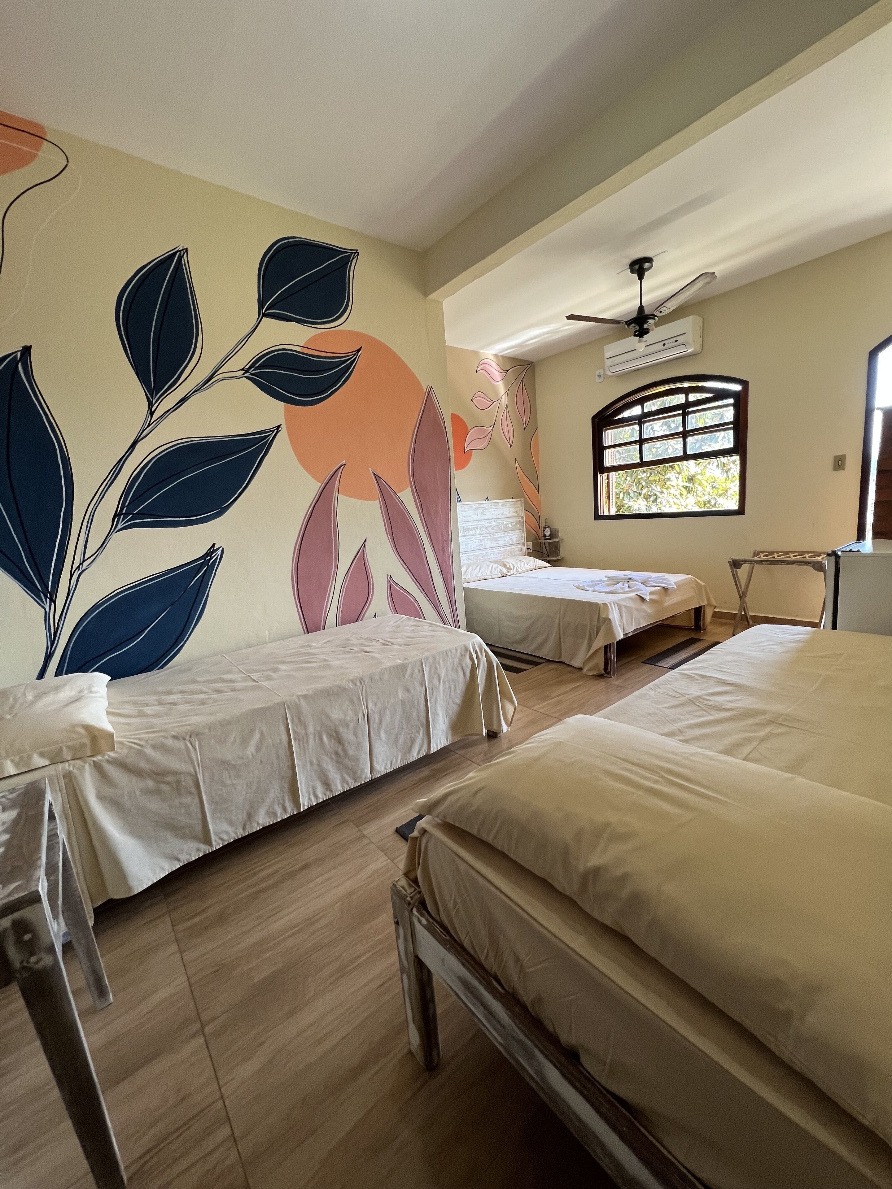 Une chambre d’hôtel avec deux lits, un ventilateur de plafond, un appareil de climatisation et une fenêtre donnant sur un paysage verdoyant.