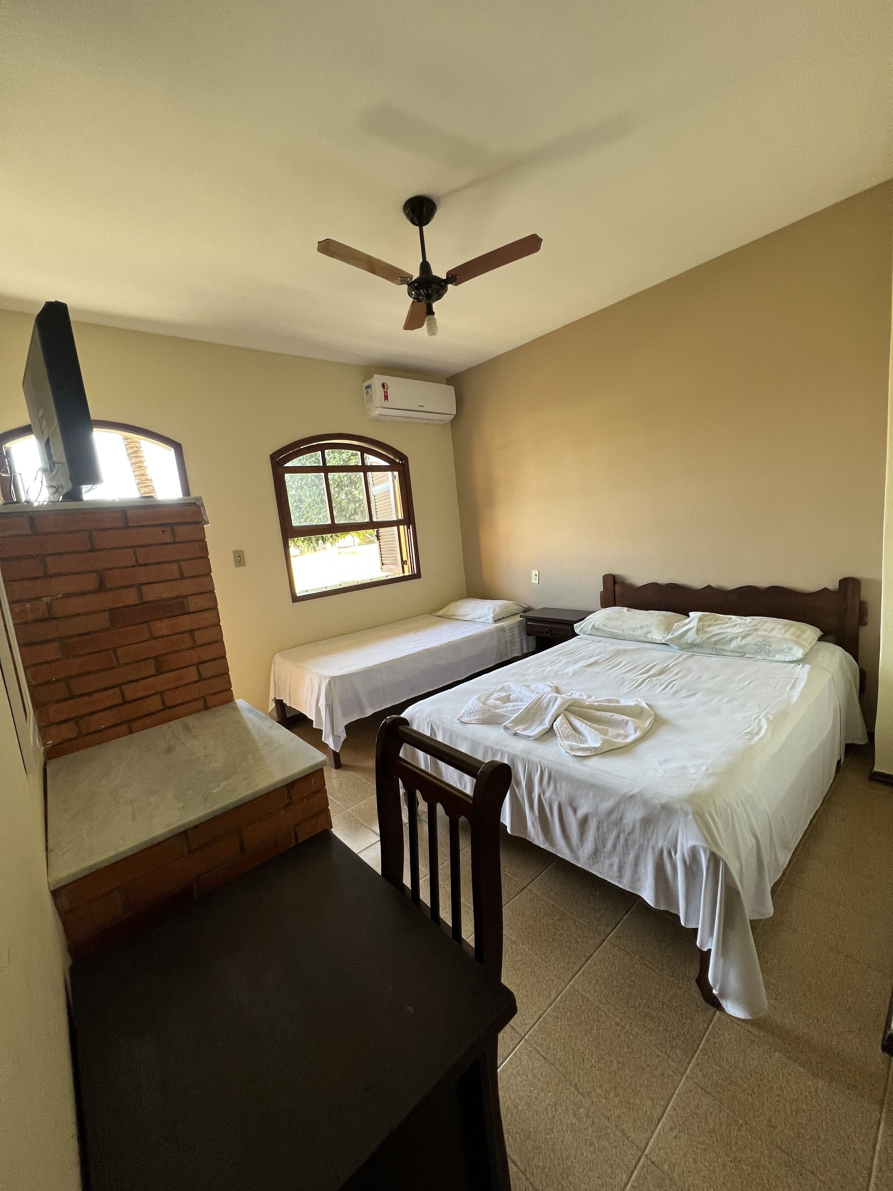 Quarto de hotel com duas camas, lareira de tijolos, ventoinha no teto e ar condicionado.