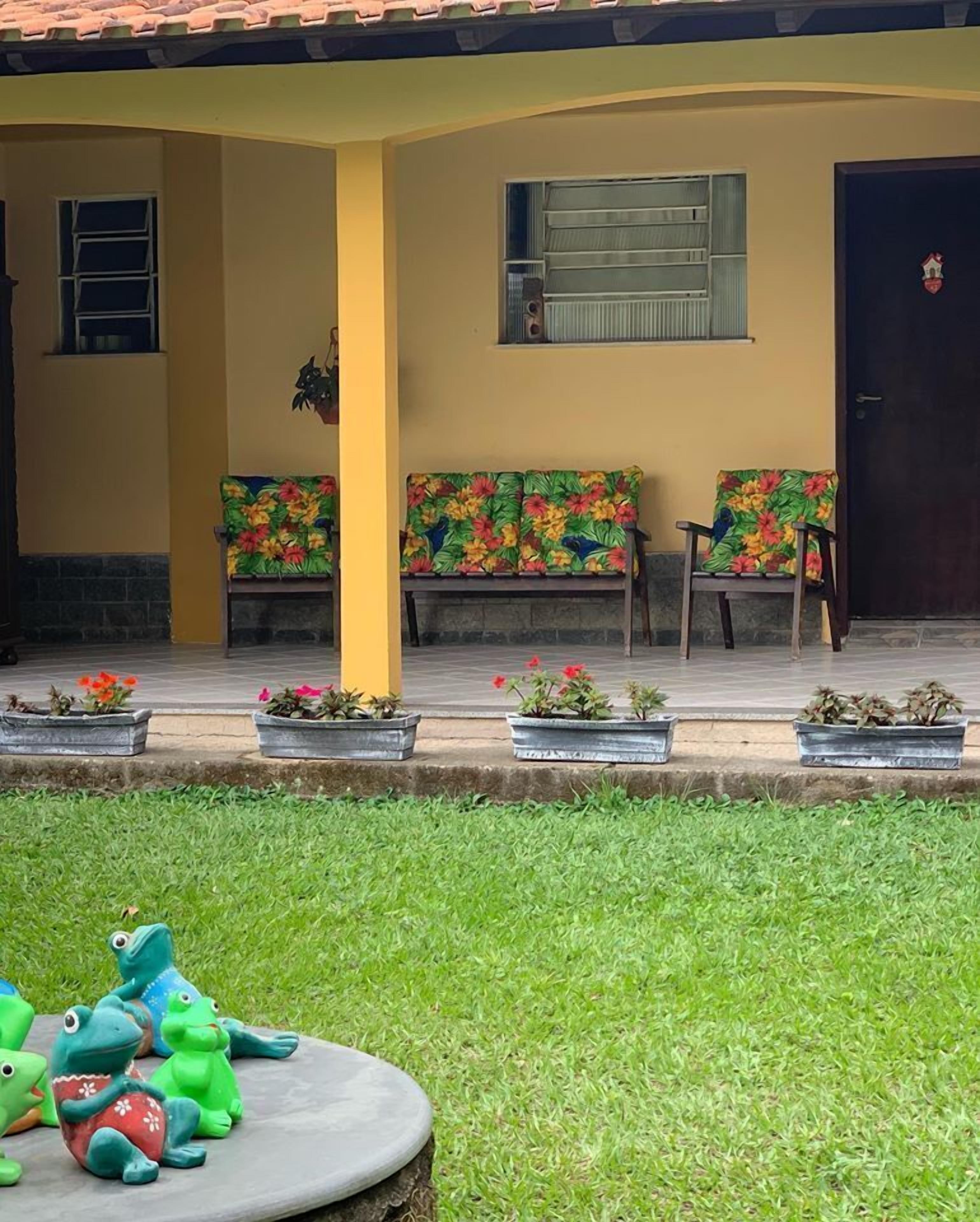 A building with a yellow facade, a covered porch with benches, and a grassy area with toy frogs.