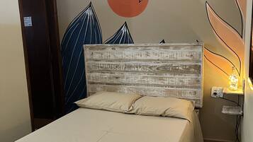 Una cama bien tendida con colcha y almohadas color beige, cabecera de madera y pared con diseño de hojas y motivo circular.