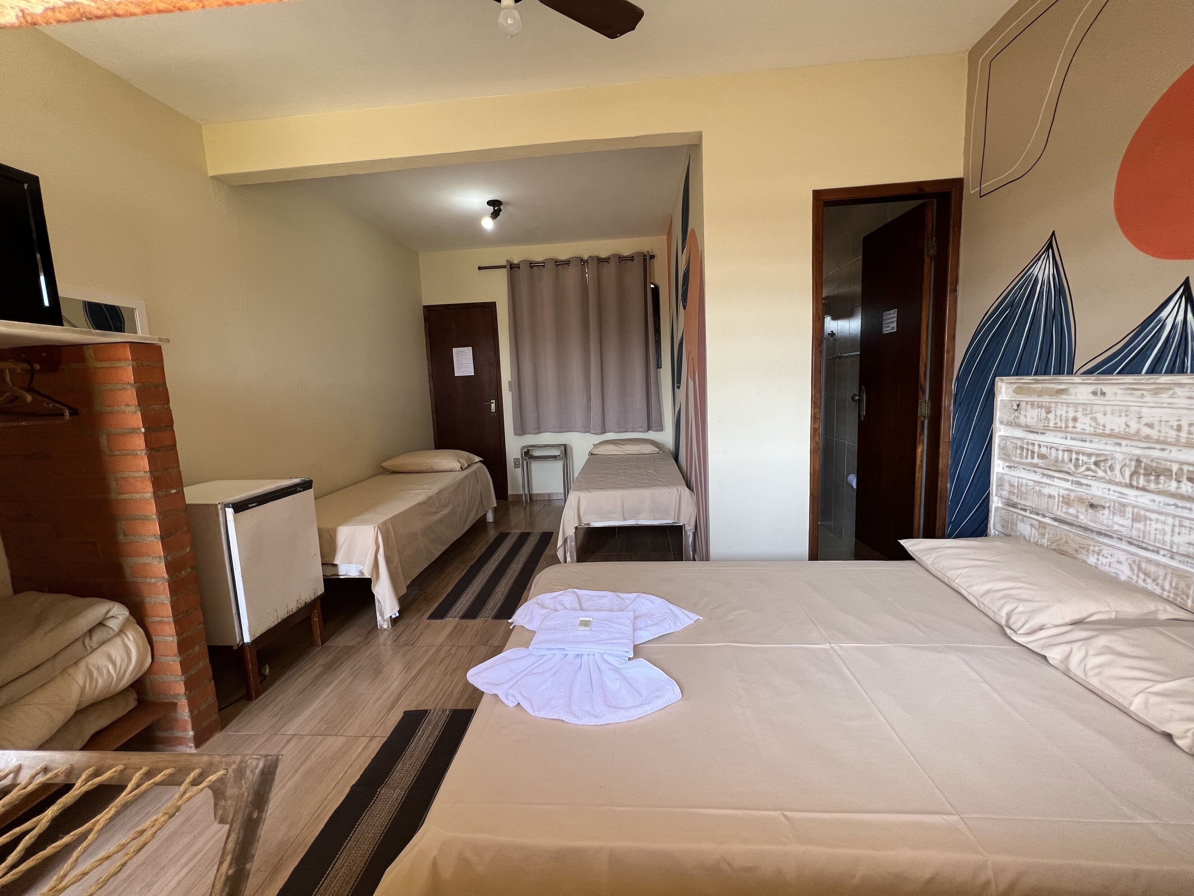 A hotel room with two single beds, a small table, a chair, a wardrobe, and a shower area.