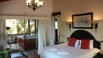 A hotel room with a bed, a balcony, a chandelier, and a painting on the wall.