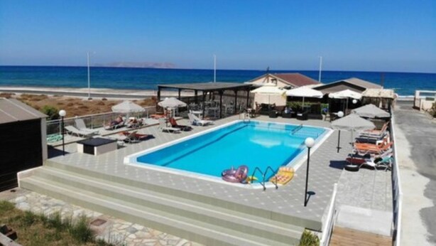 A swimming pool with lounge chairs and umbrellas, a covered seating area, and a view of the ocean. - Divina Apartments  by Estia (Hersonissos)