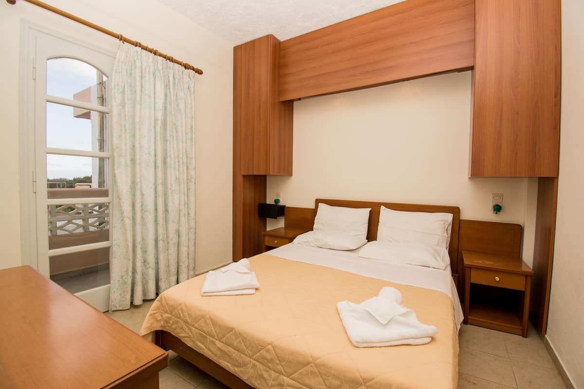 A hotel room with a bed, a wooden nightstand, a wooden headboard, a window with curtains, and a view of the outdoors.
