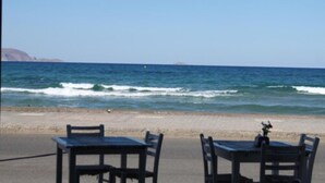 A beachside view with a table and chairs facing the ocean. - Divina Apartments  by Estia (Hersonissos)