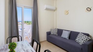 A room with a grey sofa, a dining table with chairs, and a view through a glass door. - Divina Apartments  by Estia (Hersonissos)