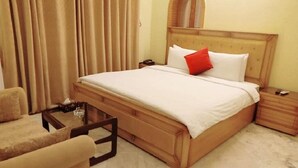 Una habitación de hotel con una cama grande, un cabecero de madera, una mesita de noche y una silla.