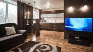 Uma sala de estar moderna com um sofá marrom escuro, uma televisão e uma cozinha ao fundo.