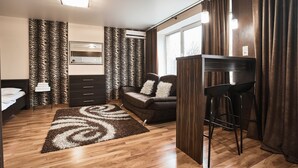 Quarto moderno com piso de madeira, sofá, escrivaninha com cadeiras e janela com cortinas.