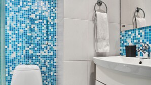 Um banheiro com vaso sanitário branco, pia com espelho e parede revestida com azulejos de mosaico azul.