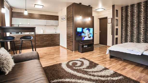 Quarto de hotel moderno com sofá, televisão, área de cozinha e parede estampada.