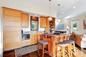 A kitchen with wooden cabinets, a bar area with stools, a large island, and a dining area with a sofa.